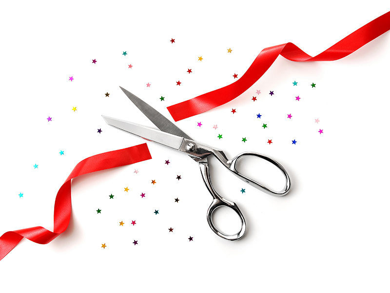 grand opening illustrated with a scissors, a red ribbon and confetti on a white background