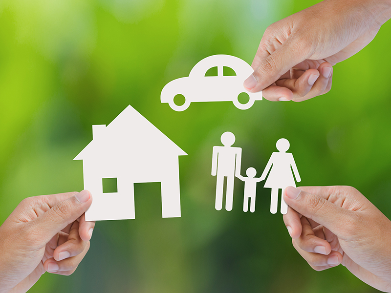 Hand holding a paper home, car, family on green background, insurance concept