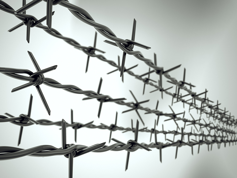 Five strands of new barbed wire forming top of fence on blurred background.