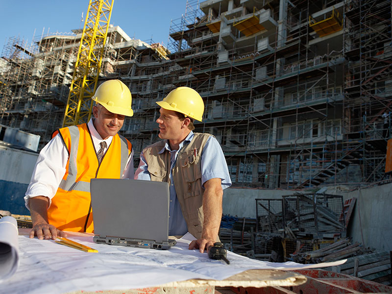 Two Men Wearing Hard Hats Looking at a Laptop Computer on a Building Site