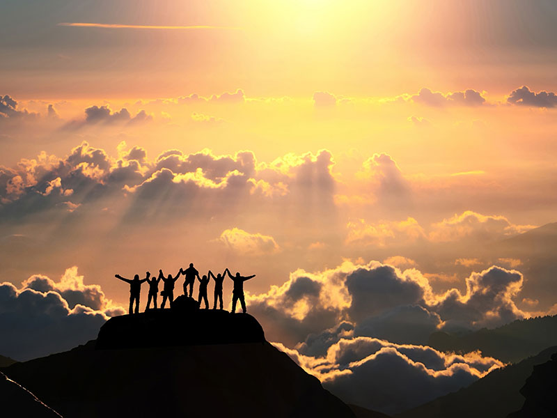 On the top of the world together. A group of people stands on a hill over the beautiful cloudscape.