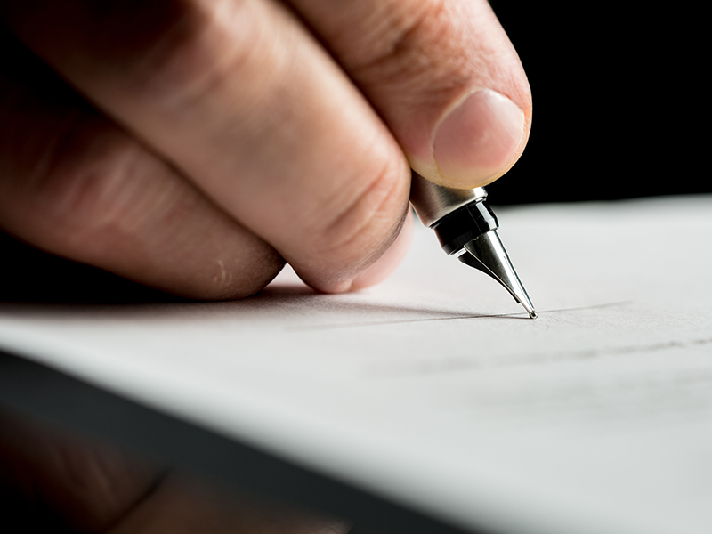 Macro shot of a hand of a businessman signing or writing a document on a sheet of white paper using a nibbed fountain pen.