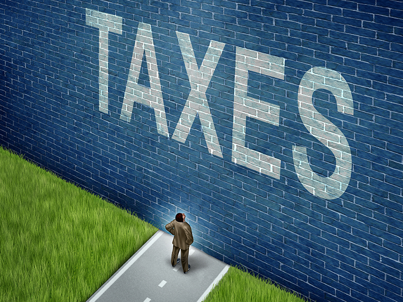 Tax problems business and financial concept as a businessman on a road to success blocked by a brick wall with the word taxes painted on the surface as a metaphor for finance issues as an adversity to growth.