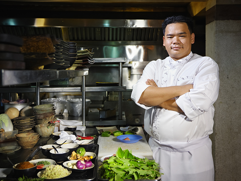 portrait of adult man at work as chef in the kitchen of an asian restaurant, posing with arms crossed