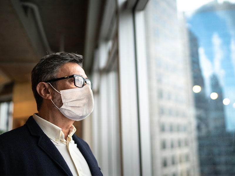 Mature businessman looking out of window with face mask stock photo