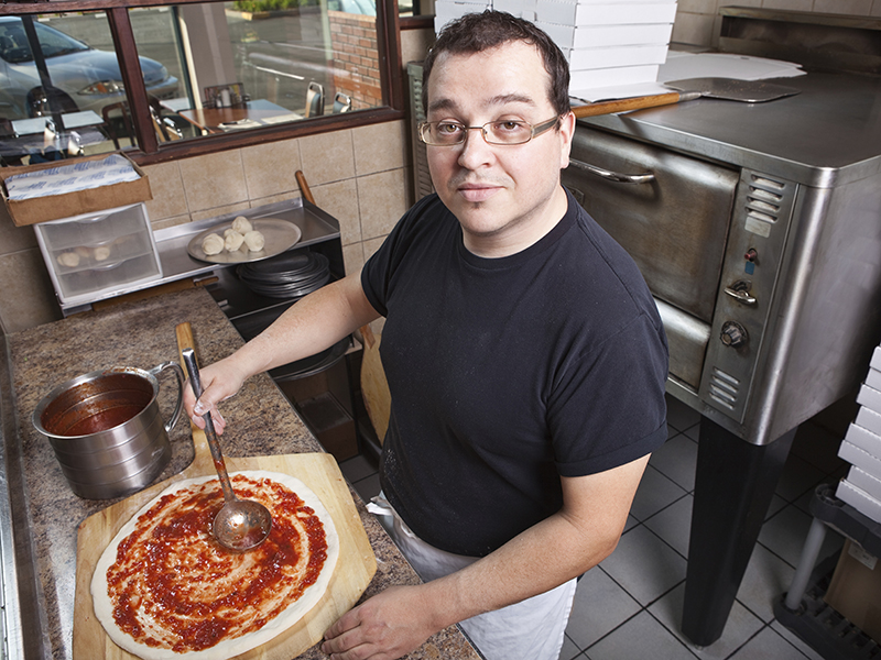 chef making a pizza spreading sauce