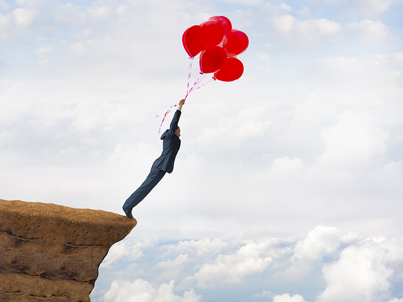 business freedom concept courageous daring businessman flying off a cliff holding faith in balloons
