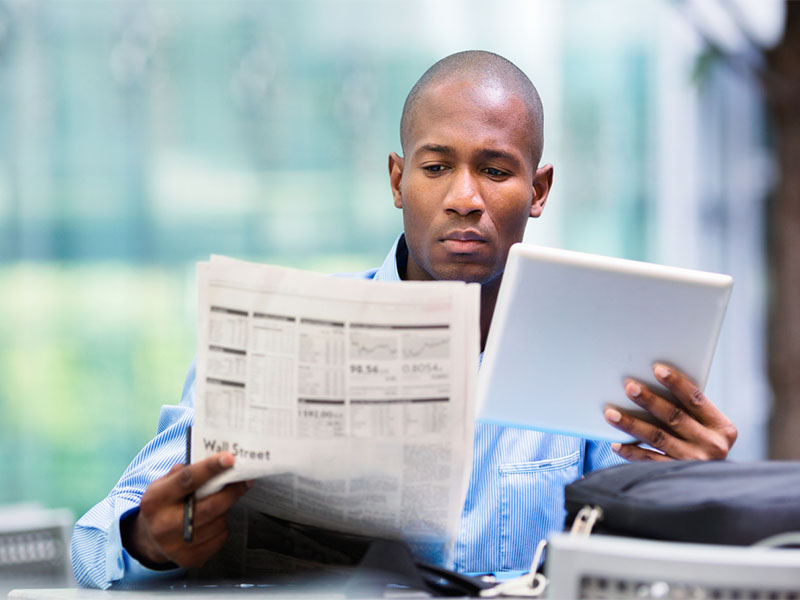 man checking stocks on newspaper and tablet