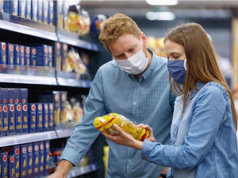 Couple wearing protective masks reading label on dried pasta in supermarket stock photo