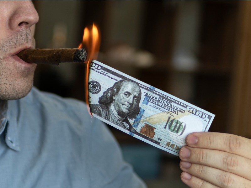 Young brutal man lighting cigar with 100 dollar bill as a symbol of wealth and success