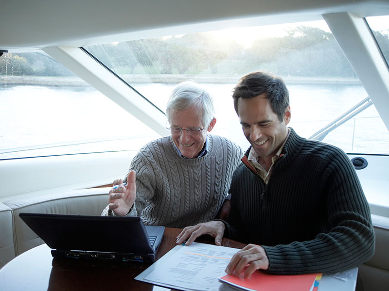 Senior and mature man sitting on yacht using laptop, smiling