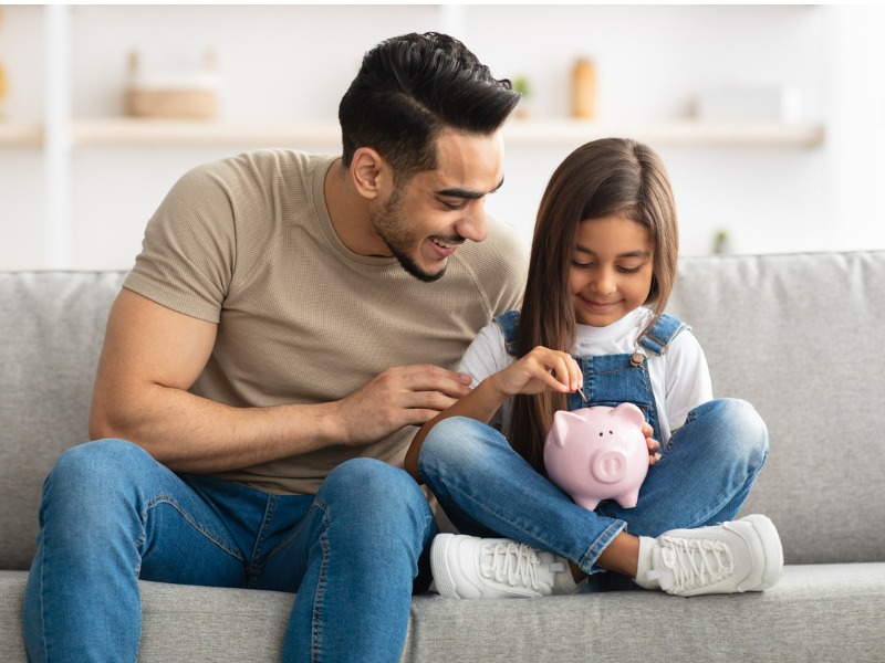Little girl and dad saving money in piggy bank stock photo