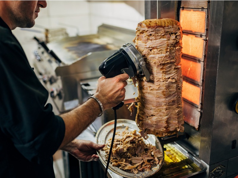 In the kitchen of the Greek restaurant, the chef using the electric tool to cut the chicken gyros from the gyros grill stock photo