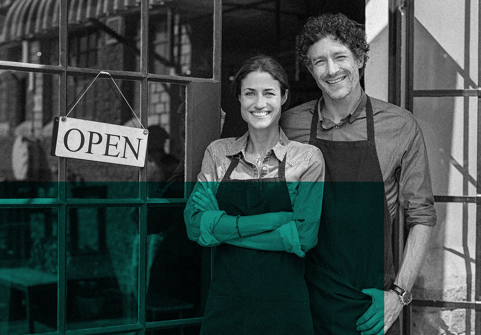 Two cheerful small business owners smiling while standing at entrance to their business
